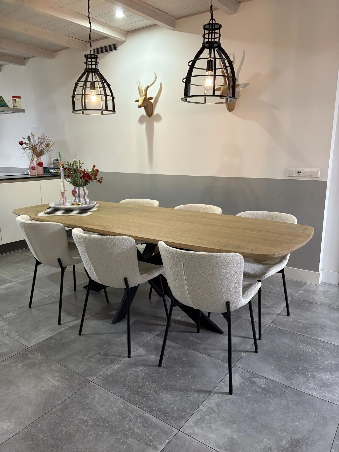 Ovale eiken eettafel met zwarte stalen poten en witte stoelen in een lichte woonkamer